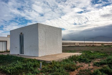 Geniş bir sera yakınında bulutlu gökyüzünün altında geleneksel bir kübik kırsal ev.