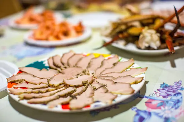 stock image A plate of sliced roasted ham and various seafood dishes on a festive table.