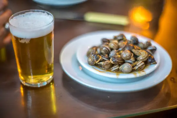 stock image A glass of beer and a plate of Andalusian-style snails, a typical tapas dish, served in a Seville tavern.