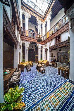 Süslü kemerler ve karmaşık ahşap özelliklerle çevrili mavi desenli seramikleri olan sakin bir avlu..