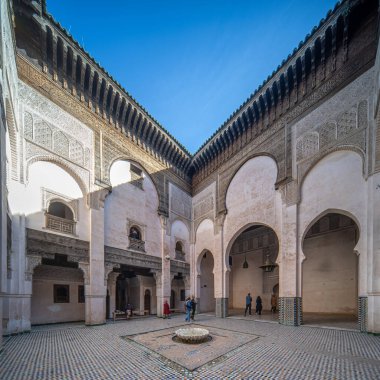 Açık mavi gökyüzünün altında Madrasa Cherratine 'in süslü avlusunda ziyaretçiler.