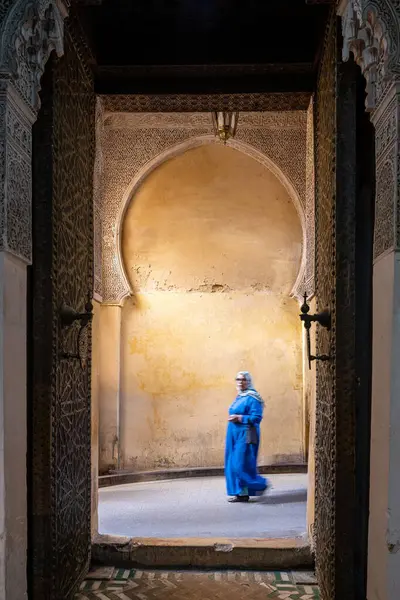 stock image A woman in blue walks through the ornate gateway of Cherratine Madrasa in Fezs ancient medina.