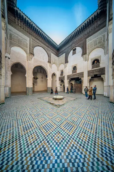 Açık mavi gökyüzünün altında Madrasa Cherratine 'in süslü avlusunda ziyaretçiler.