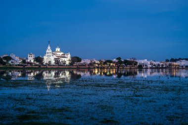 Aydınlatılmış El Rocio Kilisesi 'nin muhteşem gece manzarası Donana, Almonte, İspanya' nın sakin sularına yansıyor..