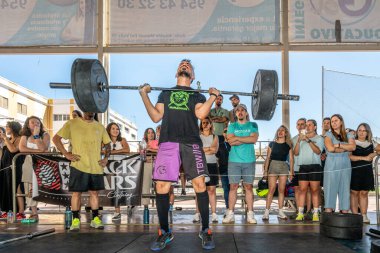 Sporcular Seville, İspanya 'da düzenlenen yoğun bir CrossFit yarışmasında halter gösterisi yapıyorlar. Kalabalık katılımcıları izliyor ve alkışlıyor.