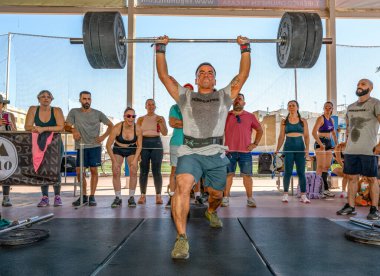Erkek sporcu, Sevilla, İspanya 'da oynanan CrossFit müsabakası sırasında arka planda tezahürat yaparak çifte alt performans sergiliyor..