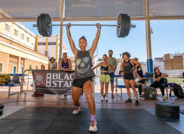 Erkek sporcu, Sevilla, İspanya 'da oynanan CrossFit müsabakası sırasında arka planda tezahürat yaparak çifte alt performans sergiliyor..