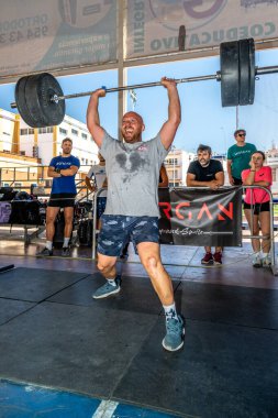 Erkek sporcu, Sevilla, İspanya 'da oynanan CrossFit müsabakası sırasında arka planda tezahürat yaparak çifte alt performans sergiliyor..