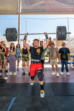 Erkek sporcu, Sevilla, İspanya 'da oynanan CrossFit müsabakası sırasında arka planda tezahürat yaparak çifte alt performans sergiliyor..