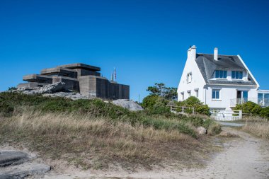 The Grand Bunker of the former German Command and Fire Direction Post in Ouistreham, Brittany, France, alongside a nearby house under a clear blue sky. clipart