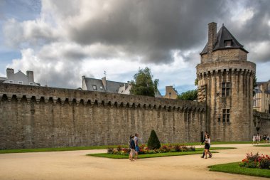 Turistler Vannes, Brittany, Fransa 'daki tarihi duvarları ve ikonik polis kulesini keşfediyorlar. Sahne bulutlu bir gökyüzü altında zengin tarihi mimariyi yakalıyor..