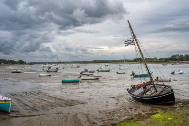 A scene of boats stranded at low tide in Vannes, Brittany, France. Overcast sky reflecting peaceful coastal charm. clipart