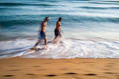 Long exposure shot capturing people walking along the shoreline of Zahora Beach in Cadiz, Spain, with waves in motion. clipart