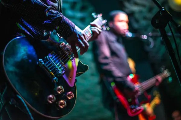 Sahnede canlı performans sergileyen gitarist ve şarkıcıyı yakından izleyin. Renkli ışıklar altında..