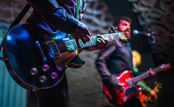 Sahnede canlı performans sergileyen gitarist ve şarkıcıyı yakından izleyin. Renkli ışıklar altında..