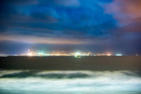 stock image Long exposure night photo of Algeciras Bay, Spain, with the illuminated Rock of Gibraltar in the background under a cloudy sky.