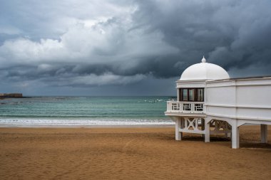 İspanya, Endülüs 'ün başkenti Cadiz' deki Playa De La Caleta plajındaki ikonik Balnear De La Palma hamamı dramatik bulutlu bir gökyüzünün altında..