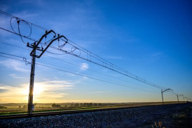 Carrion de los Cespedes, Sevilla 'daki demiryolu manastırlarının huzurlu günbatımı manzarası. Siluetli elektrik hatları, sakin bir gökyüzü tarafından vurgulandı.