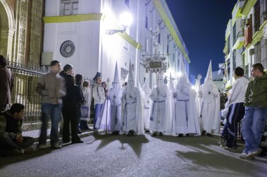 Nazarenos from the Resurrected Brotherhood during Easter Sunday morning procession in Seville, Spain. Nighttime religious tradition with spectators watching. clipart