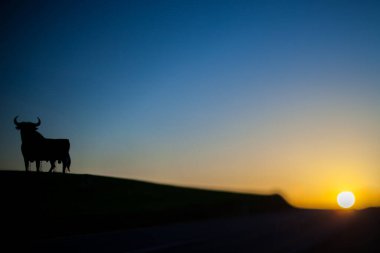 Tilt-shift lens photo of the Osborne Bull silhouette against a vibrant sunset in Seville, Spain. Peaceful and iconic scene. clipart