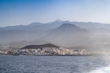 İspanya 'nın Tenerife kentindeki uzak Teide' nin yer aldığı denizden Los Cristianos manzarası. Sisli bir gökyüzünün altında sakin bir kıyı atmosferi.