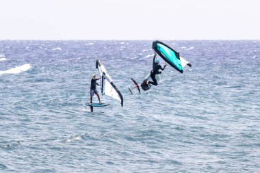 El Medano, Tenerife, İspanya 'da okyanusta güçlü dalgalar ve açık gökyüzüyle heyecan verici kanat çırpma manevraları sergileyen iki sporcu..