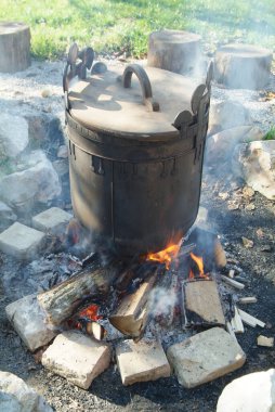 Antik Macar tarzı açık hava demir kazanı dumanlı bir kamp ateşinin üstünde.