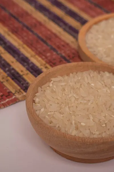 Tahta kasede çiğ pirinç ve beyaz arka planda izole edilmiş ahşap hasırın üzerine saçılmış pirinç yığını. Bir grup saf çiğ pirinç çiftçiler tarafından toplandı. Ahşap tabakta pirinç modern konsept fotoğrafçılık.