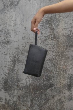 Bir kadının eli siyah kozmetik bir keseyi dokulu bir arka planda izole edilmiş bir fermuarla tutar. Siyah çanta kozmetik.