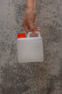 Bir kadının eli, izole edilmiş bir arka planda çeşitli sıvıları taşımak için küçük bir bidon tutuyor..