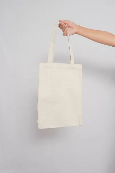 El ele tutuşan bej renkli tuval çanta beyaz arka planda izole edildi. Çanta Beyaz Arkaplan Beyaz Boş Renk.