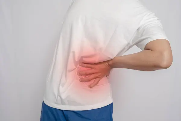 Beyaz tişörtlü bir adam elini belinde ağrı, kalçasında ağrı ve beyaz arka planda ağrı ile tutuyor..