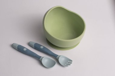 Silikon kaşık ve çatalı olan yeşil bir kase, bebekle beslenmek için ayarlanmış, beyaz bir arka planda izole edilmiş..