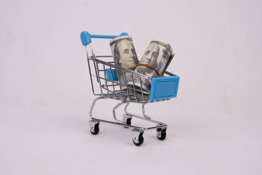 Minyatür mavi bir alışveriş arabası resmi ve beyaz izole edilmiş bir arka planda dolar banknotları. İnternetten alışveriş konsepti. Nakit olmayan ödeme yöntemleriyle alışverişin kolaylığı.