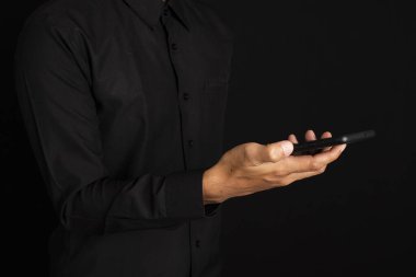 İşadamının orta kısmı, siyah arka planda dururken akıllı telefon kullanıyor..