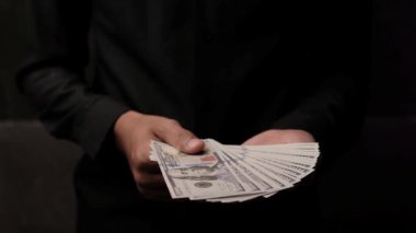 Tanınmayan siyah elbiseli bir adam avucuna bir tomar para sıkıştırdı. Yakın mesafeden. Para adamın elinde. Finansal konsept, para birikimi. Yüksek kalite 4k kayıt.