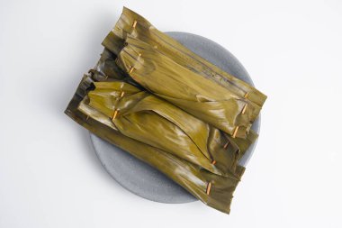 Pepes Tahu Jamur, baharatlı tofu ve mantar, muz yapraklarına sarılı, sonra buğulama ve ızgara. Ahşap masa veya motif tabakta servis ediliyor.