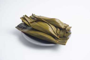 Pepes Tahu Jamur, seasoned tofu and mushroom, wrapped in banana leaves then steamed and then grill a while.  Serving on wooden table or motif plate. clipart