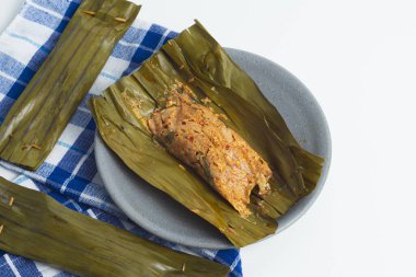 Pepes Tahu Jamur, seasoned tofu and mushroom, wrapped in banana leaves then steamed and then grill a while.  Serving on wooden table or motif plate. clipart