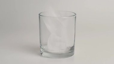 Buz küpleri beyaz arka planda boş bir bardağa düşüyor. Buz parçaları çift duvarlı bir bardağa düşer. Yakın plan..
