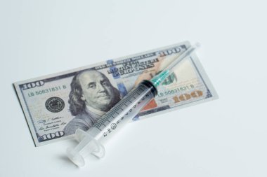 Beyaz arka planda dolar üzerine şırınga. Sağlık hizmetlerinin pahalı olduğu fikri. Toplumda hastane masraflarının çok pahalı olduğu komplosu..