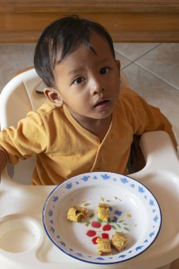 Toddler 'ın tost yerken yakın çekim. Mutlu Asyalı çocuk sandalyesinde peynir ve yumurta ile tost kahvaltısı yapıyor. Küçük çocuk kahvaltısını yüksek sandalyesinde ve masasında yapıyor..