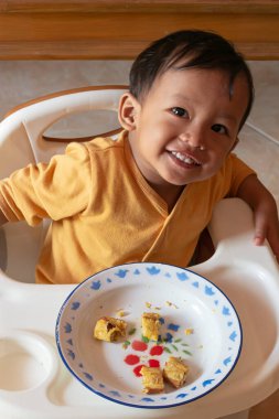 Toddler 'ın tost yerken yakın çekim. Mutlu Asyalı çocuk sandalyesinde peynir ve yumurta ile tost kahvaltısı yapıyor. Küçük çocuk kahvaltısını yüksek sandalyesinde ve masasında yapıyor..