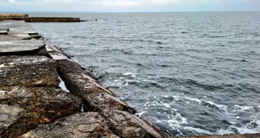 Arka planda eski taş duvar ve deniz.