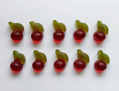  Beyaz arka planda parlak şekerler. Yeşil yapraklı kırmızı kiraz şeklinde desenli jöle şekerler.