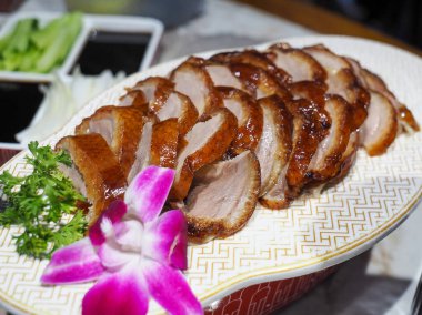 Çin desenli seramik tabakta Pekin ördeği taze salatalık, yeşil soğan, kişniş ve süslü çiçeklerle servis edilir..