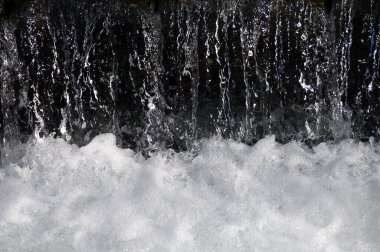 Karanlık bir zemin üzerinde bir dağ deresinde küçük şelaleler siyah ve beyaz bir gölge ve ışık efekti yaratır.