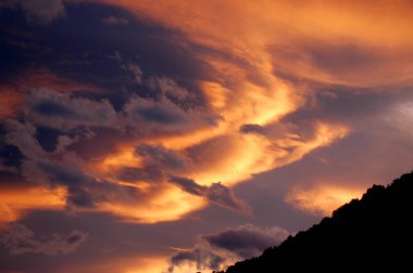 Dağlarda gün batımında pembe kırmızı ve morla aydınlanan bulutlar.