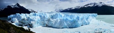 Patagonya 'daki Perito Moreno Buzul Cephesi' nin geniş ekran görüntüsü. Arka planda kristal mavi buz oluşumları ve karla kaplı kayalık dağlar var.
