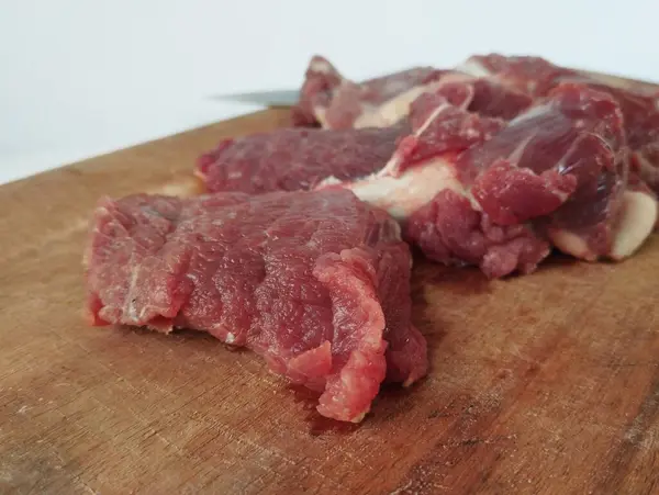 Stock image Raw beef meat on a wooden cutting board and beside it is a knife, on the festival of sacrifice during Eid al-Adha Al Mubarak isolated on a white background.